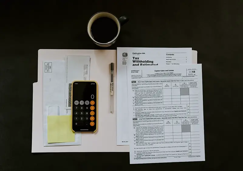Open document folder containing tax information next to calculator, pen and cup of coffee