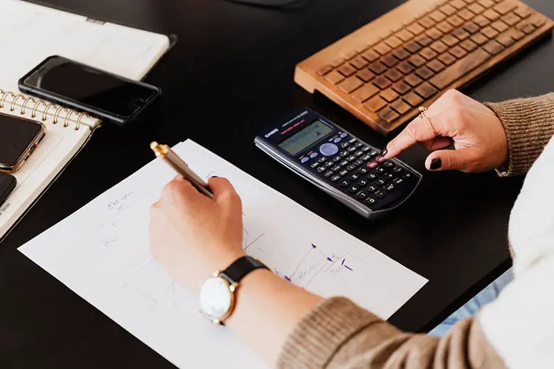 Woman using calculator and taking notes on paper