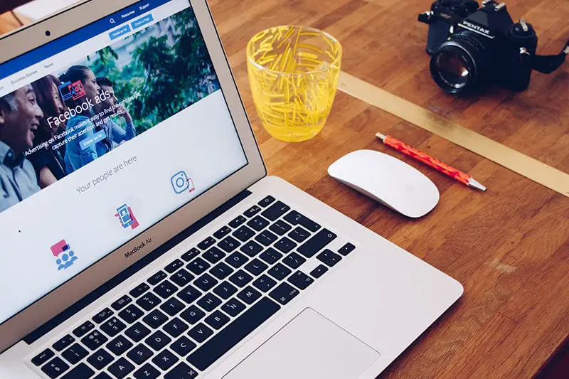 A laptop with facebook on screen and camera on the top of wooden table