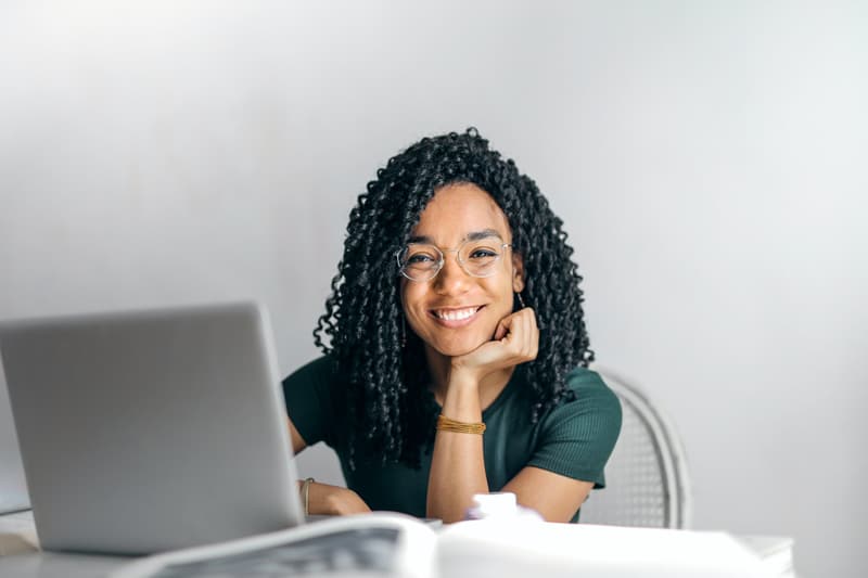 happy ethnic female student sitting at a table with laptop 