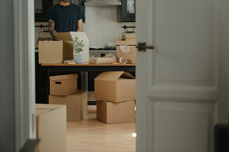 man in black tshirt standing next to brown cardbox boxes in an office