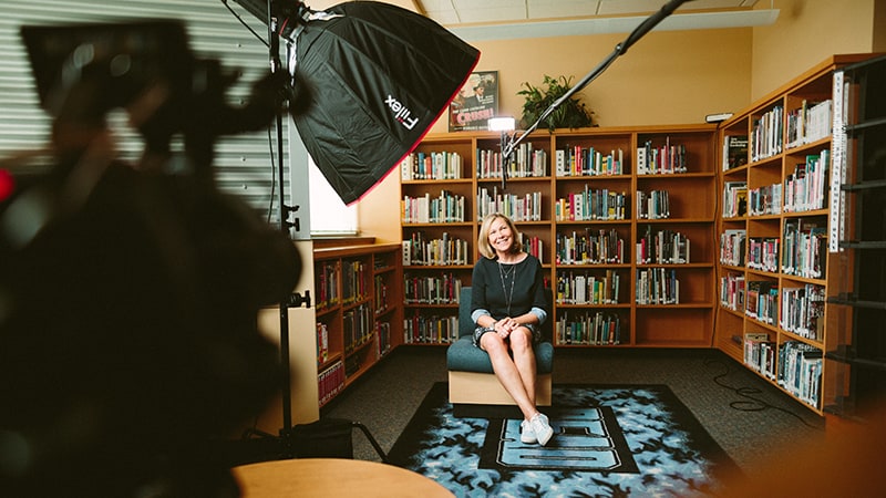 woman sitting on chair in library - video marketing content being recorded