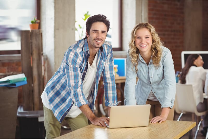 2 employees standing side by side in front of laptop on table in a small business office
