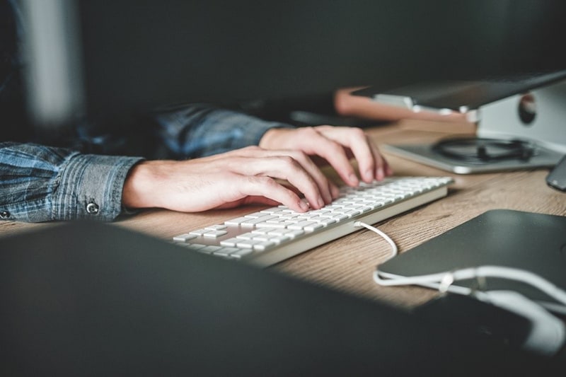 A person with long sleeves polo typing in white keyboard