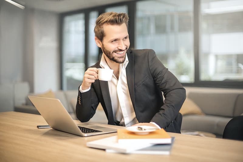 Man holding white teacup in front of a gray laptop