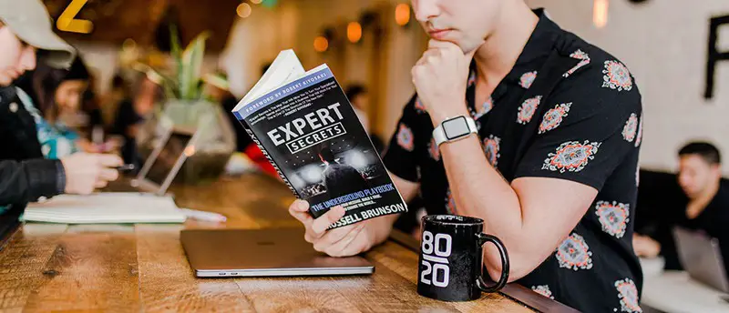 A person in black reading a book and black coffee mug beside him