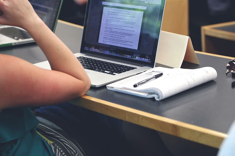 Person studying English course on macbook computer, with notebook to the side