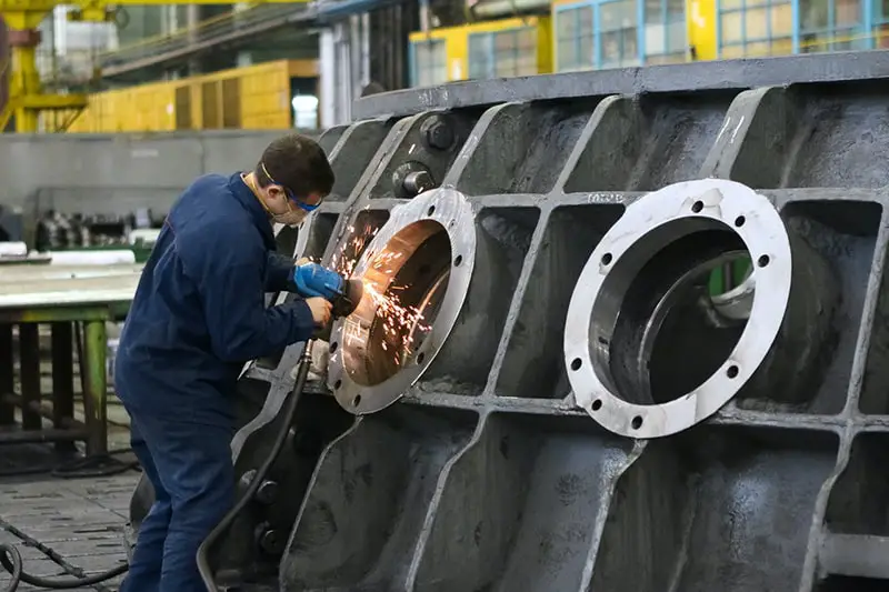 man welding round window frame in manufacturing company