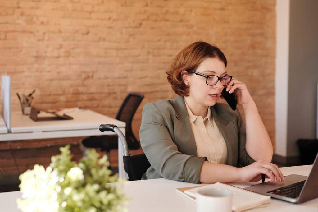 woman talking on samrtphone while using laptop