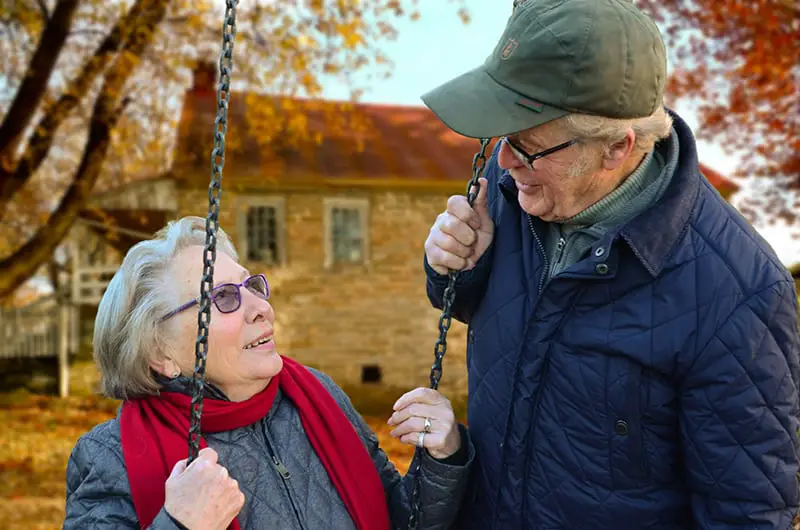 An old man standing beside old woman on swing