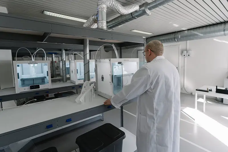 man in white laboratory gown in front of 3d printer