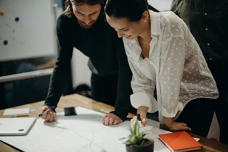 Man and woman leaning on table staring at white board on top of the table