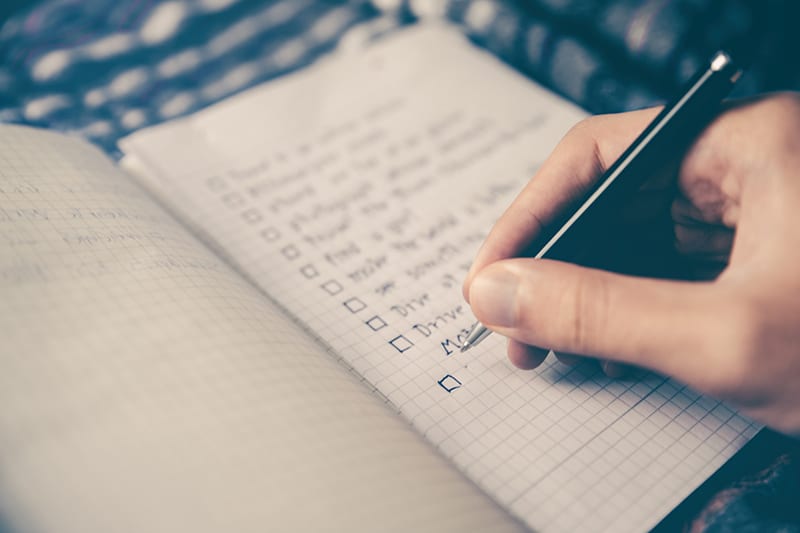 person writing notes checklist in notebook