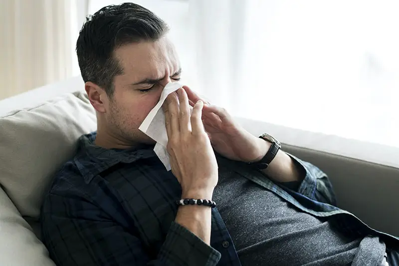 A man sneezing while lying on the sofa