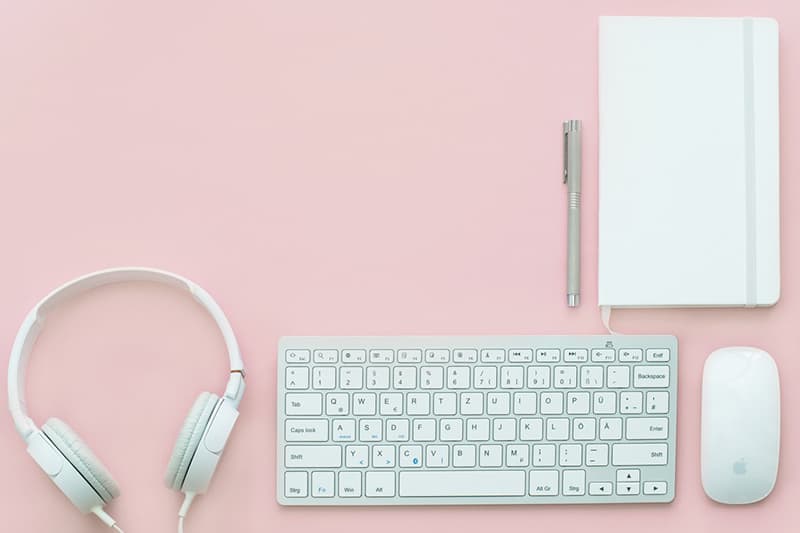 White apple mouse, keyboard, headphones, notebook, and pen