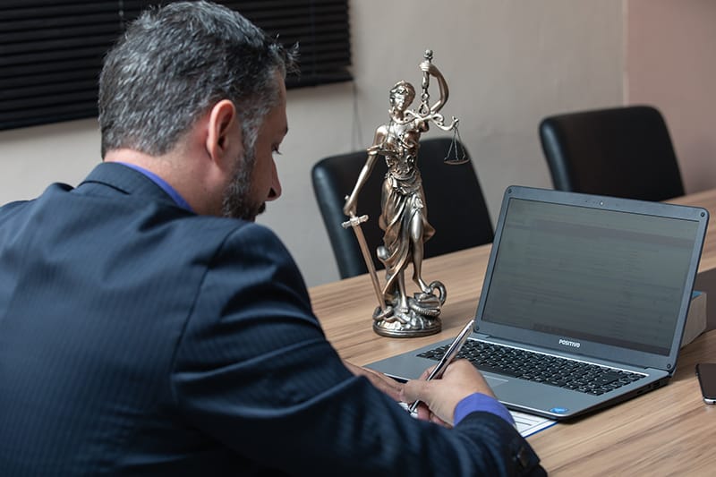 A lawyer writing on the paper while in front of laptop