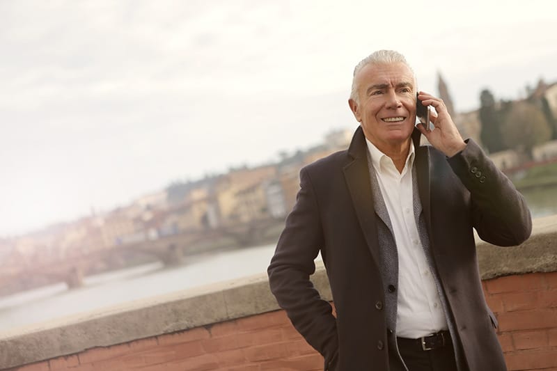 A man in a suit standing next to a brick wall speaking on mobile phone