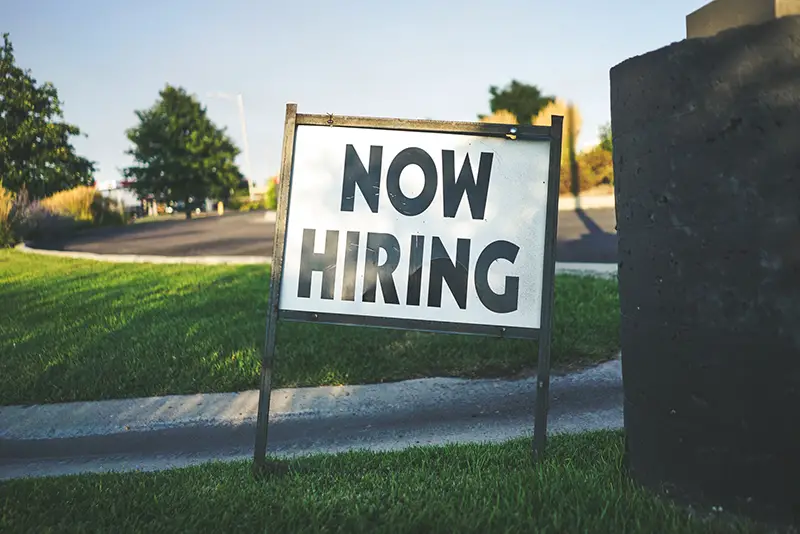 Black and white Now Hiring sign on grass