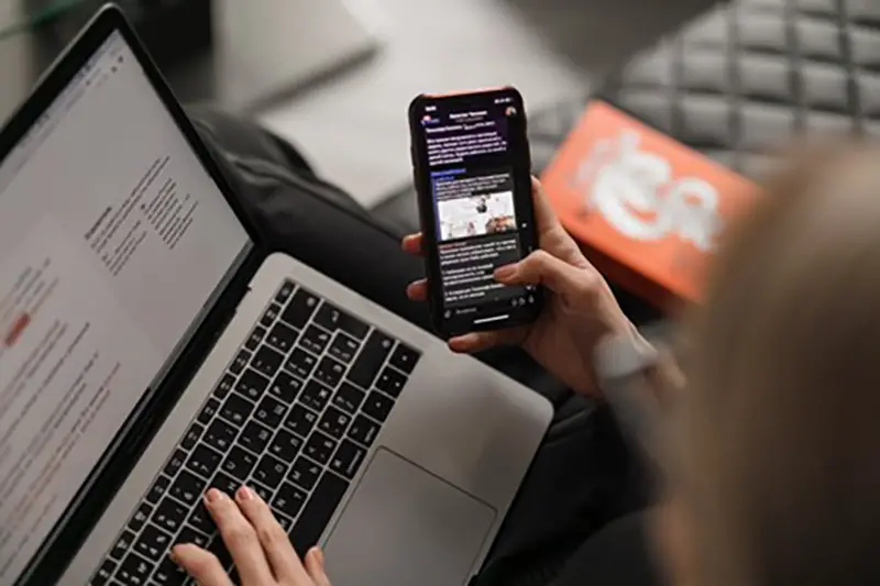 A person using laptop while holding black smartphone