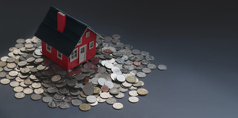 Carton miniature house placed on table with stack of coins