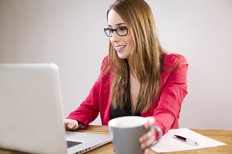 Woman using laptop while holding mug