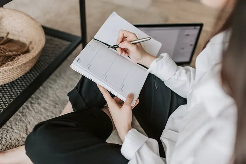 Woman writing in notebook while sittig in the couch