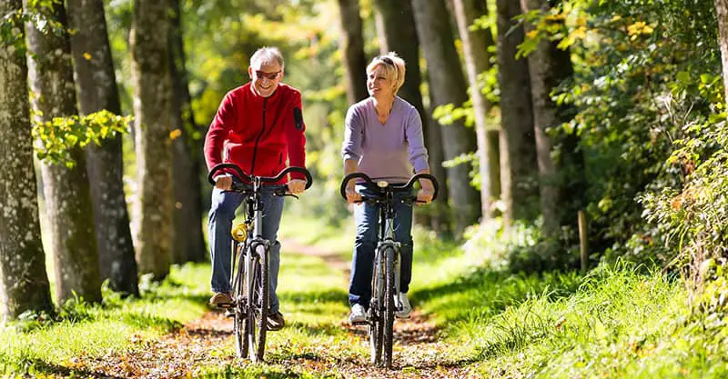 Two people cycling in woodland enjoying their retirement