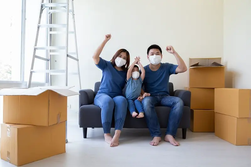 Family wearing mask sittingon sofa next to packed boxes in new home