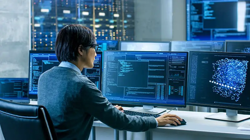 Technical Operator Works at His Workstation with Multiple Displays Showing Graphics