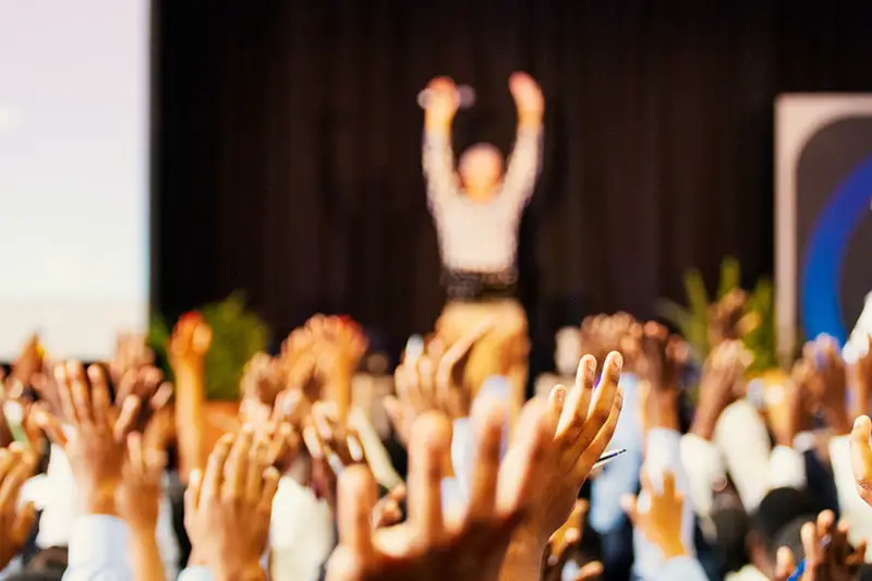 conference room full of people with their hands raised at an event