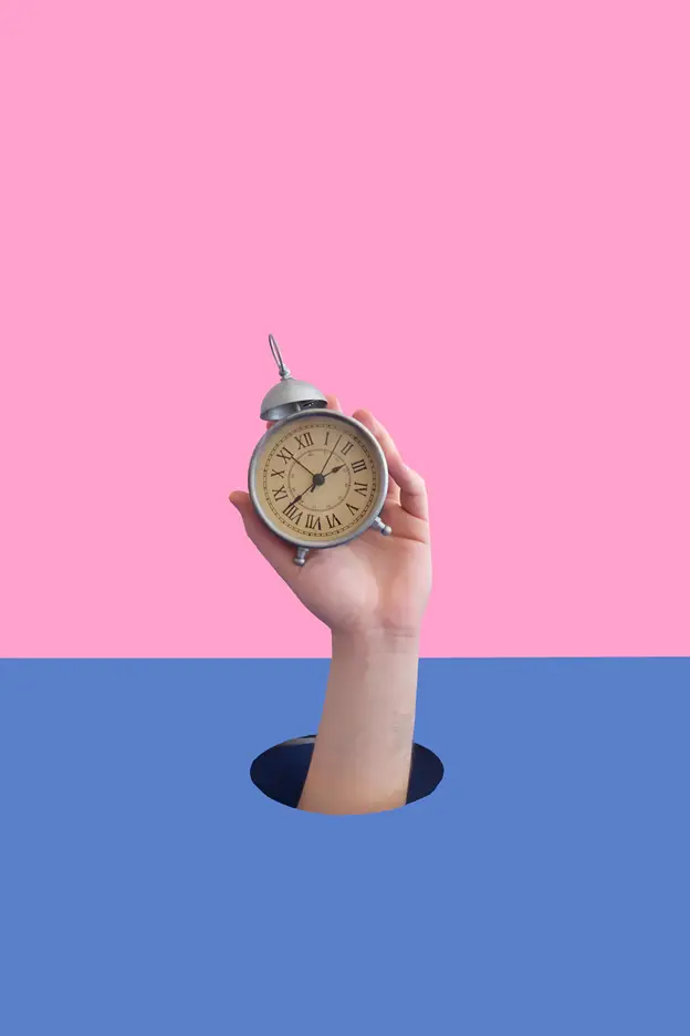 Hand holding an alarm clock – pink and blue background