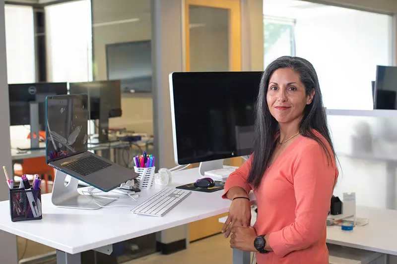 Businesswoman in long sleeved orange top next to her standing desk