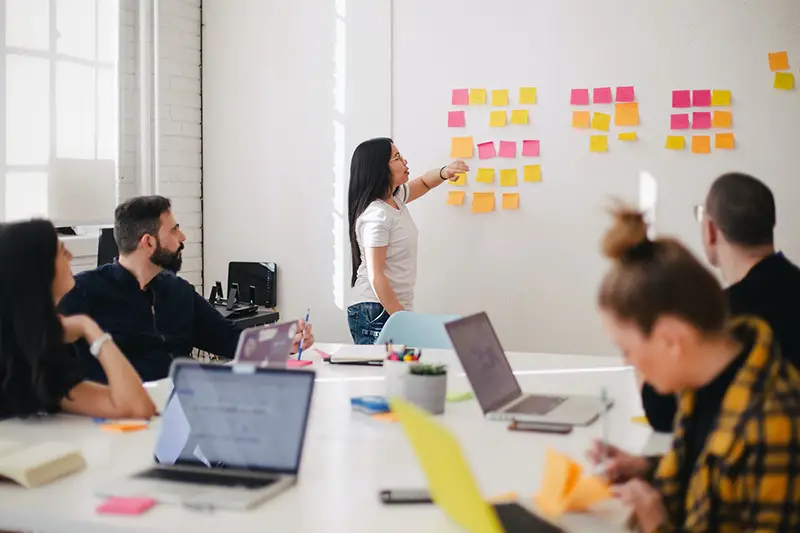 woman placing sticky notes on wall in business meeting