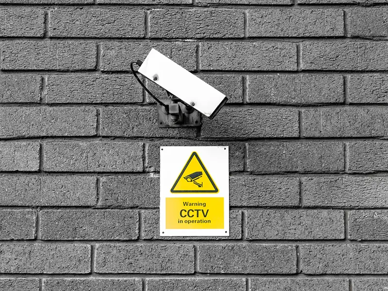CCTV camera on grey wall with yellow sign