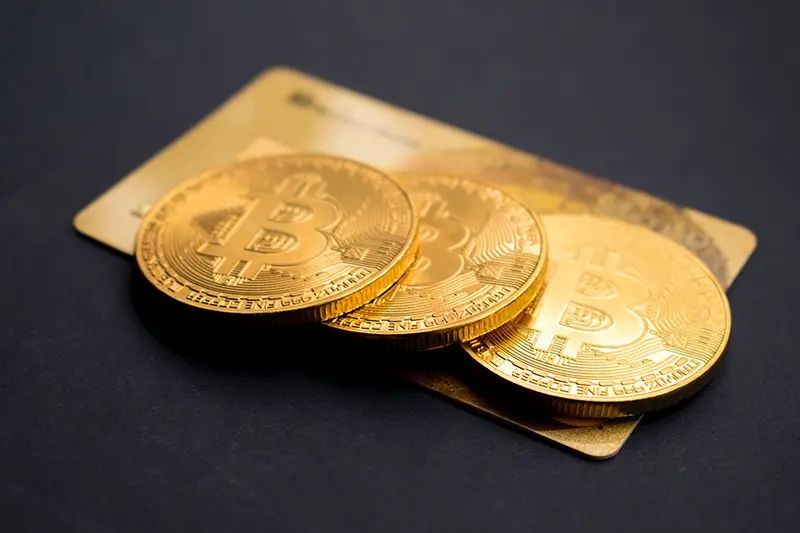 Three gold coloured bitcoin tokens on top of a gold credit card and black table