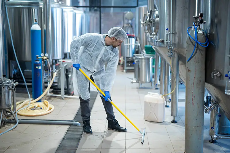 Professional industrial cleaner in protective uniform cleaning floor of food processing plant. Cleaning services.