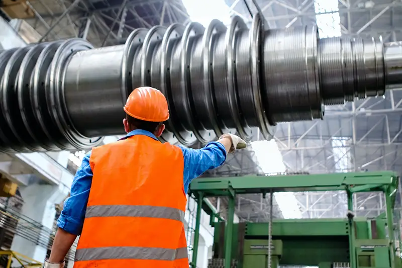 Man wearing orange hard hat and high visibility vest while inspecting equipment