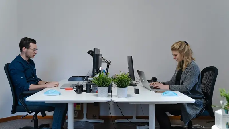 two people in an office working on laptops