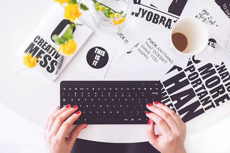 Woman wearing red nail polish typing on the black keyboard