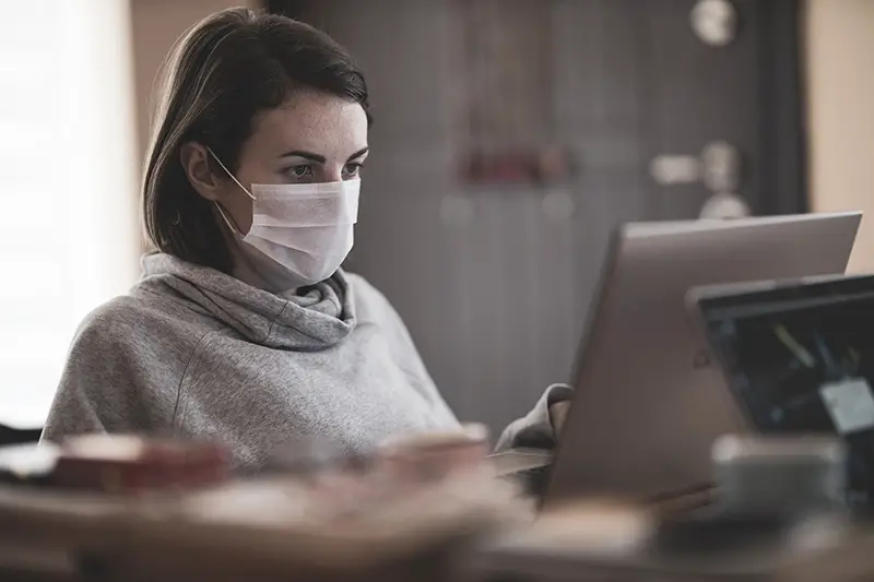 Woman working on her laptop while wearing facemask