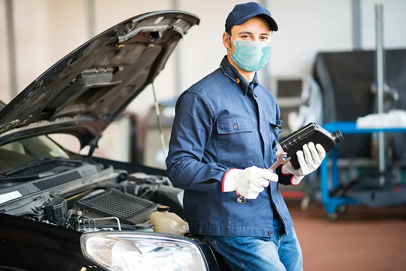 Masked car mechanic holding a jug of motor oil