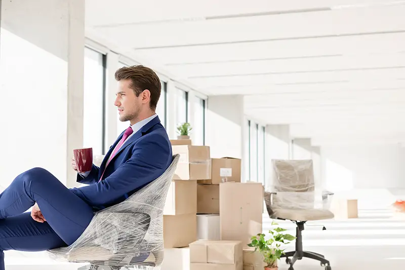 Side view of young businessman having coffee on chair in new office