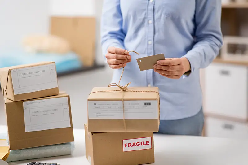 woman packing parcel box and tying tag by rope at post office