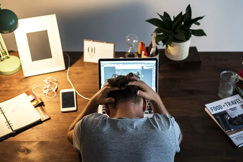 Man holding his head while in front of his laptop