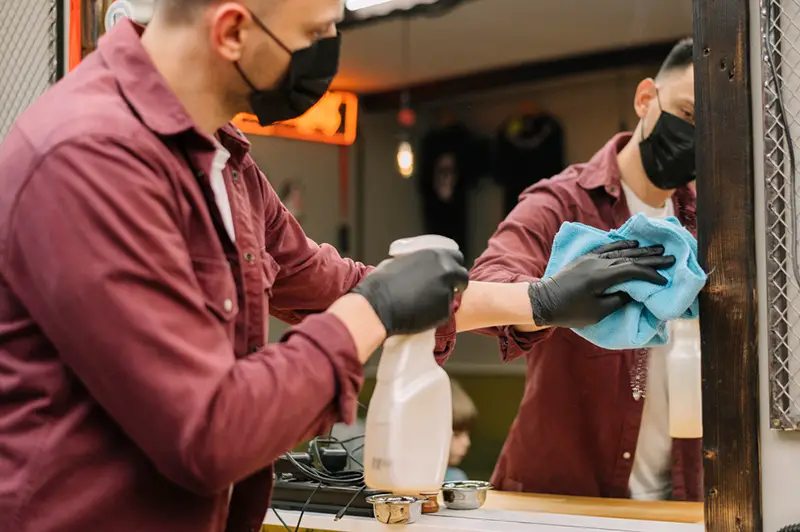 Salon worker wearing mask and gloves sanitizing surfaces using salon disinfectant