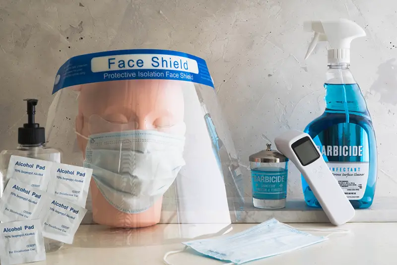 Items to be used for clean and sanitizing the salon next to a dummy head wearing face mask and face shield