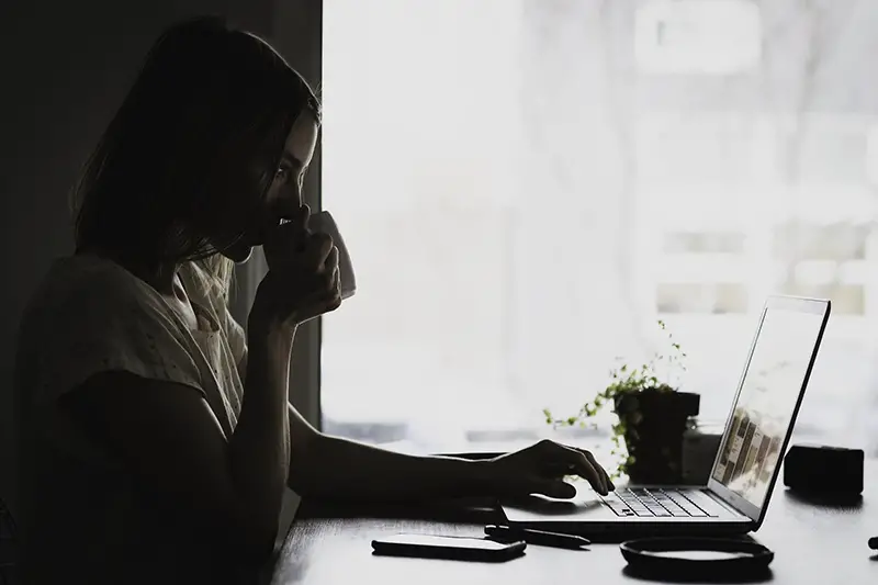 Woman drinking coffee while working on her laptop