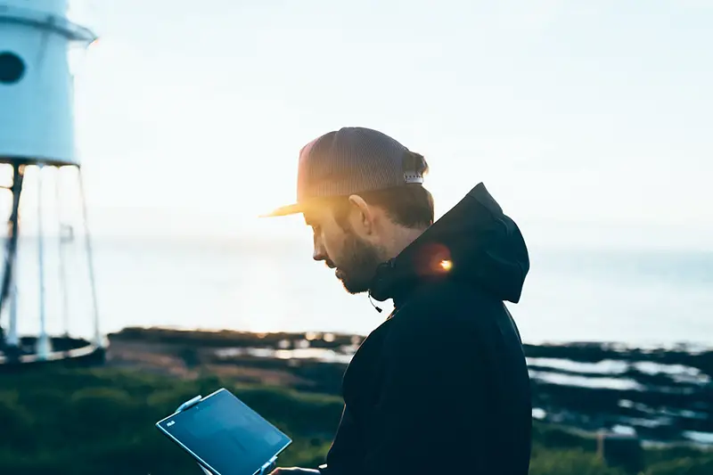 Young man wearing black jacket and cap near seaside