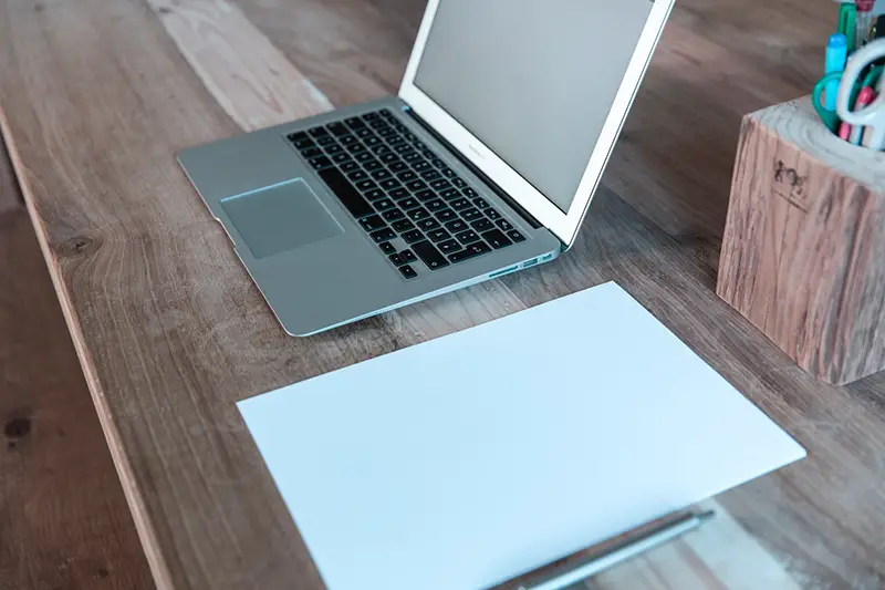 MacBook Pro on a wooden table next to a note pad and pen