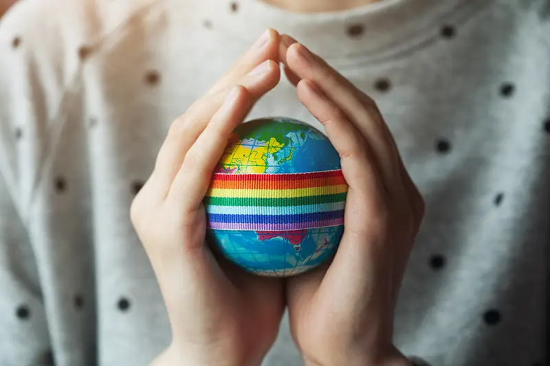 woman's hands holding globe with LGBT rainbow ribbon